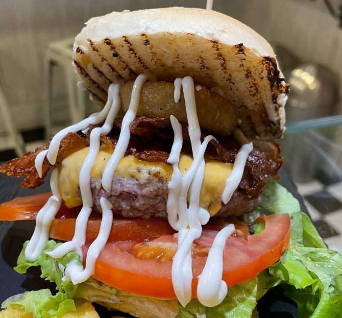 Il cheeseburger Arnold's con bacon, cheddar fuso, anello di cipolla e maionese che cola